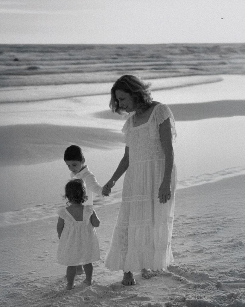 Black and white photo of a grandmother walking along the beach with her two granddaughters during a 30A extended family photography session.