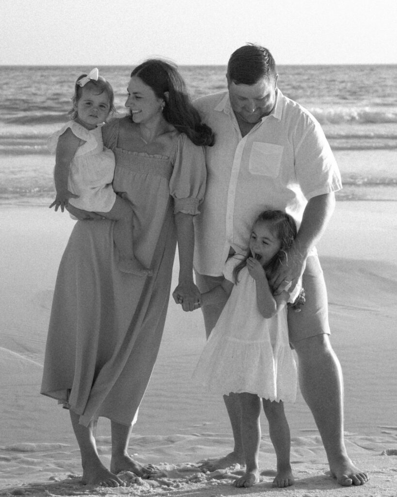 Family of four standing on the beach with seagulls flying overhead during a 30A extended family photography session.