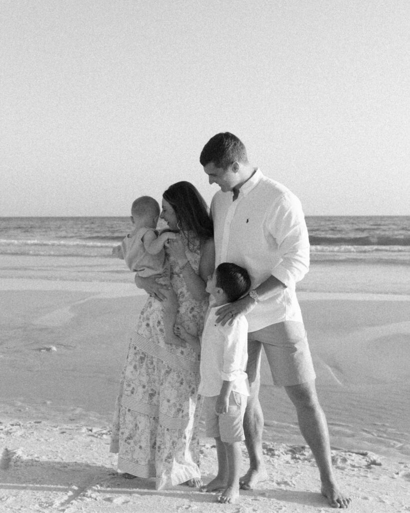 Black and white photo of parents embracing their children on the beach during a 30A extended family photography session.