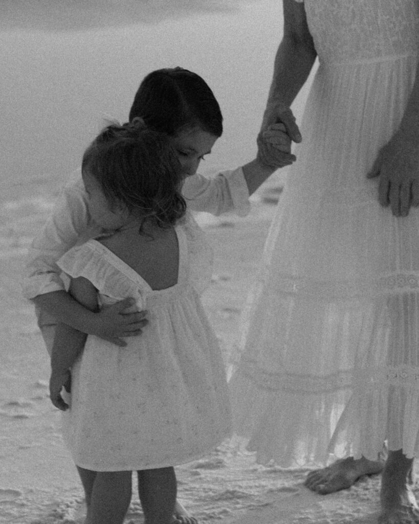 Black and white photo of a young child holding her mother’s hand on the beach during a 30A extended family photography session.