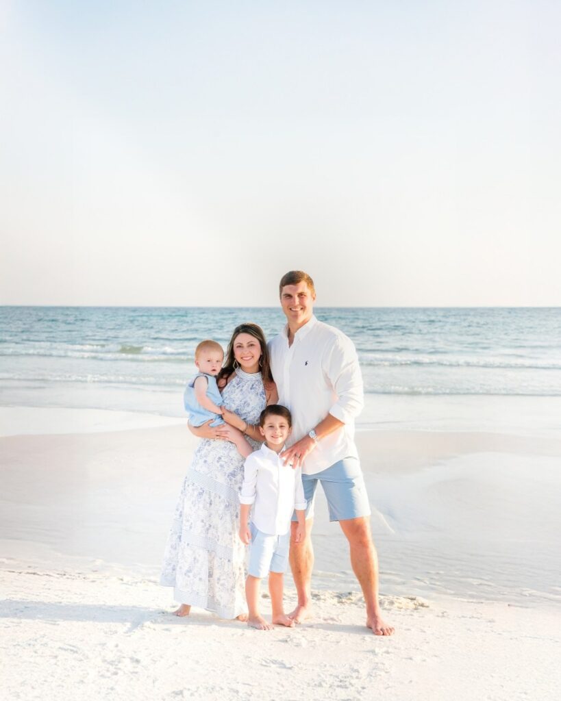 Family of four standing on the beach with seagulls flying overhead during a 30A extended family photography session.