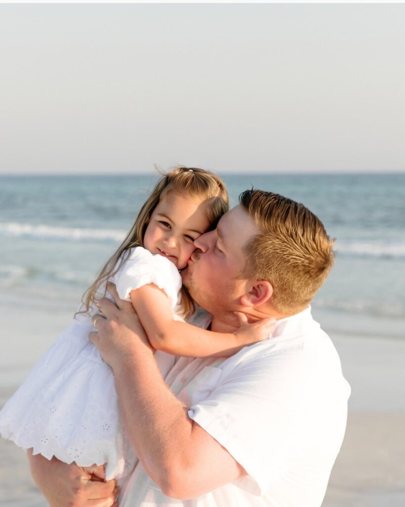 Father kissing his young daughter on the beach during a 30A extended family photography session.