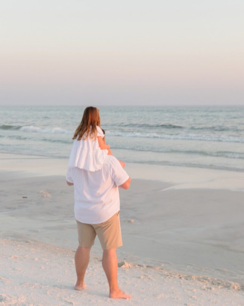 Little girl sitting on her father’s shoulders while walking along the shoreline during a 30A extended family photography session.