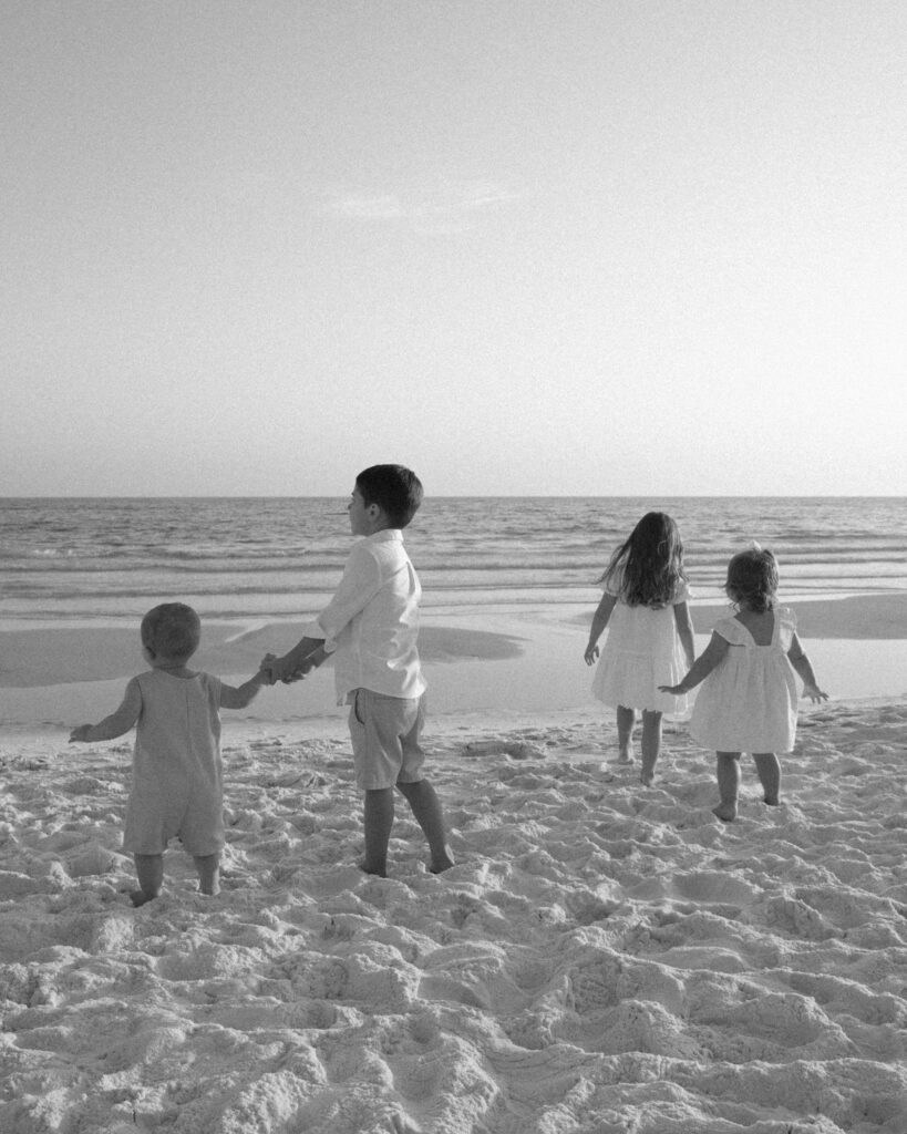 Children walking toward the ocean during a black and white 30A extended family beach photography session.