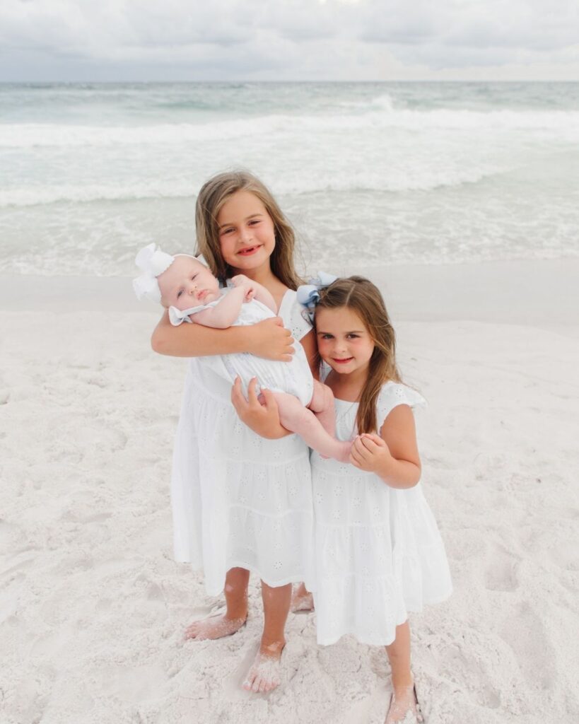 Sisters holding their newborn baby sister during a beach family session in Destin Florida