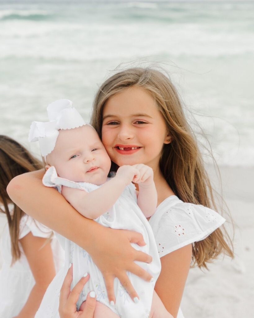 Sisters holding their newborn baby sister during a beach family session in Destin Florida