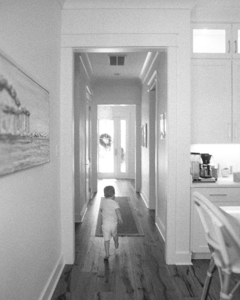 Toddler sibling walking down the hallway during an in-home lifestyle newborn session in Santa Rosa Beach Florida