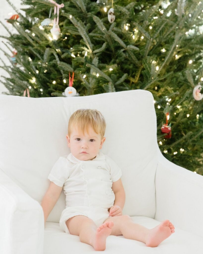 Toddler sibling reading a Christmas book in front of the Christmas tree during an in-home lifestyle newborn session in Santa Rosa Beach Florida