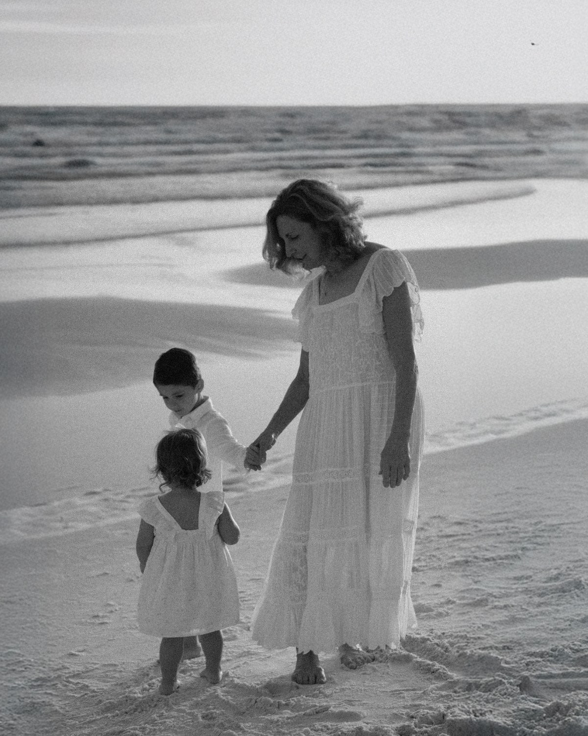 Black and white photo of a grandmother walking along the beach with her two granddaughters during a 30A extended family photography session.