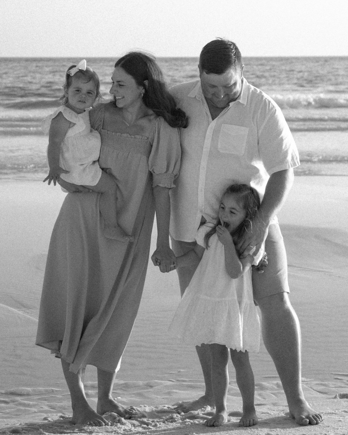 Family of four standing on the beach with seagulls flying overhead during a 30A extended family photography session.