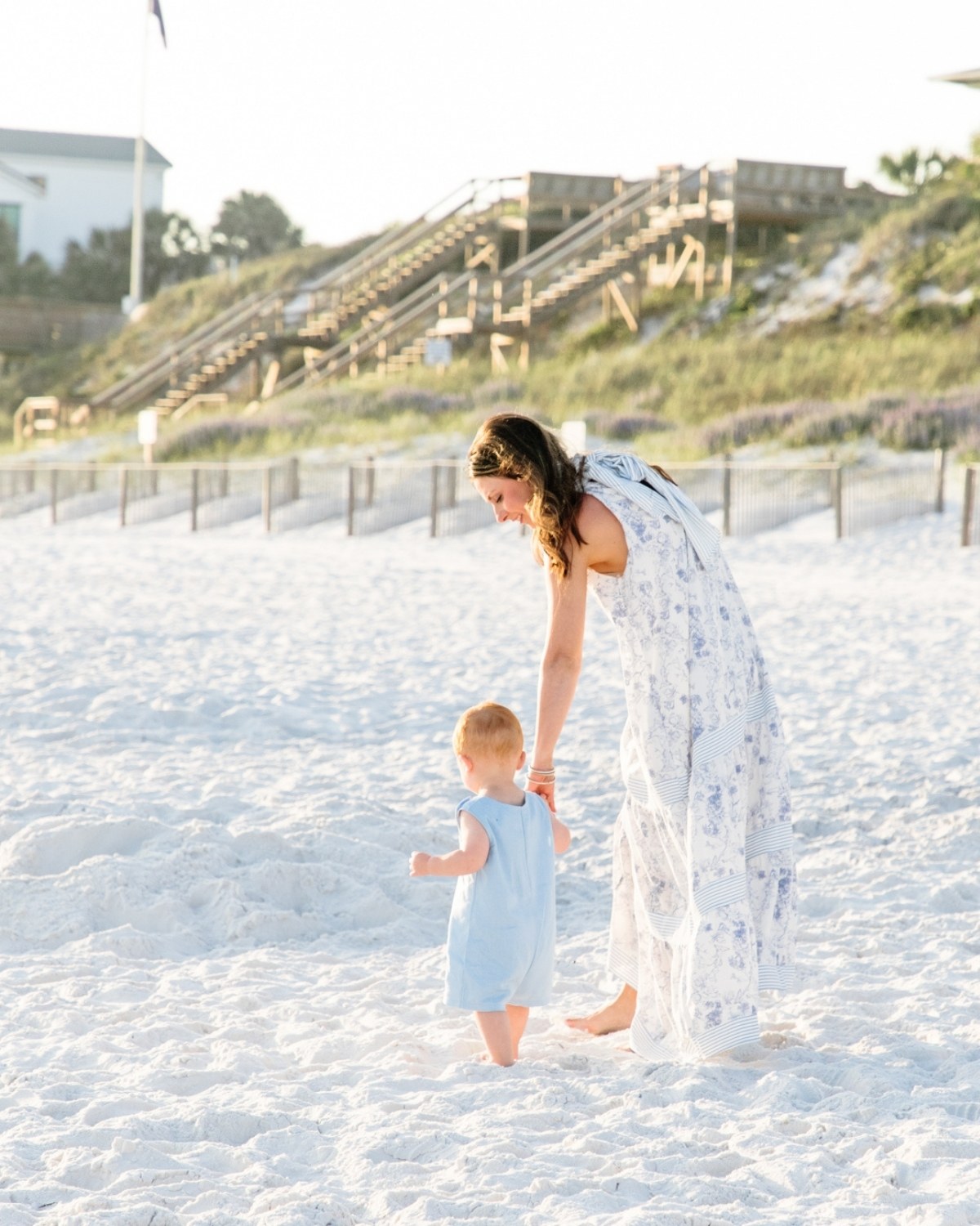 Mother bending down to help her toddler walk on the beach during a 30A extended family photography session.