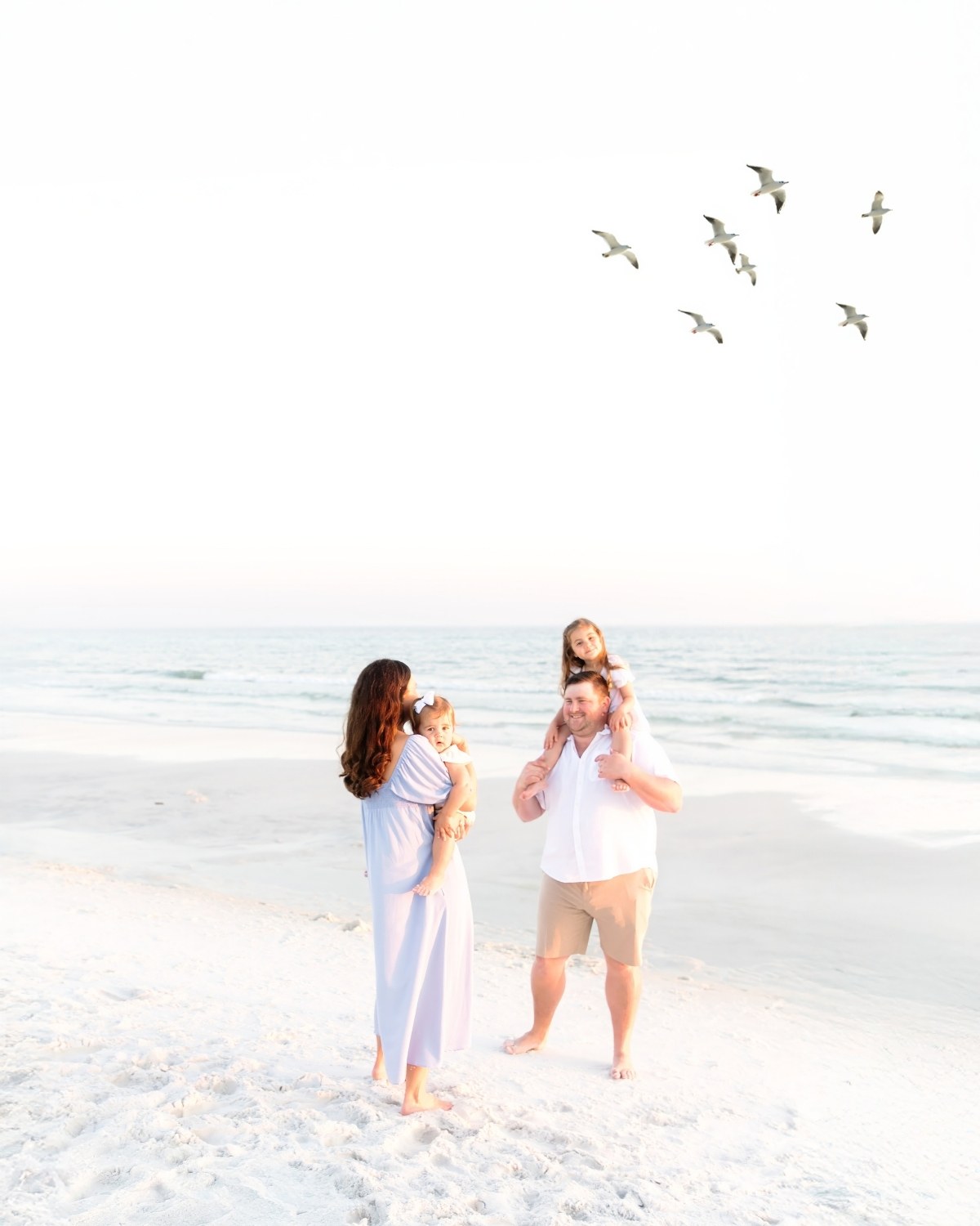 Family of four standing on the beach with seagulls flying overhead during a 30A extended family photography session.