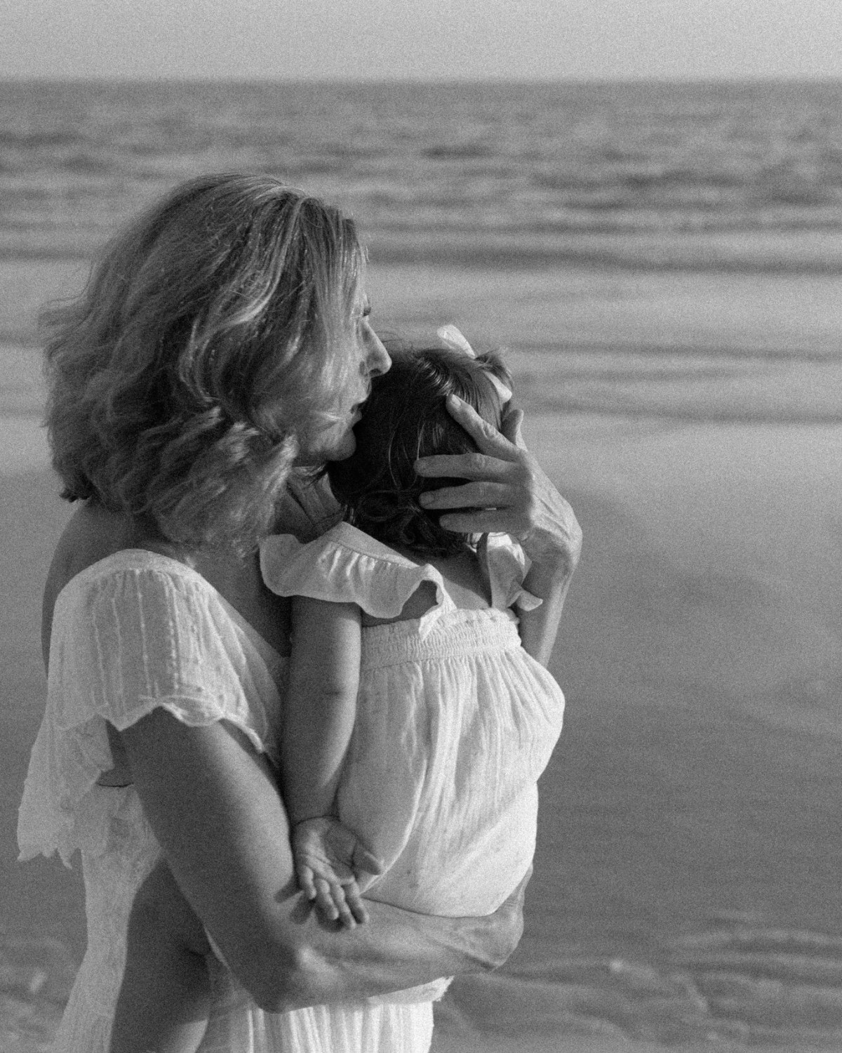 Black and white photo of a grandmother holding and comforting her grandchild on the beach during a 30A extended family photography session.